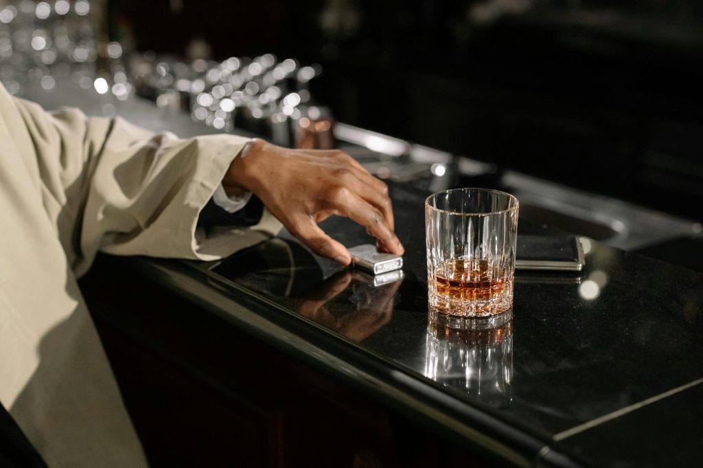 A sophisticated scene featuring a glass of whiskey and a hand reaching for a lighter at a bar counter.